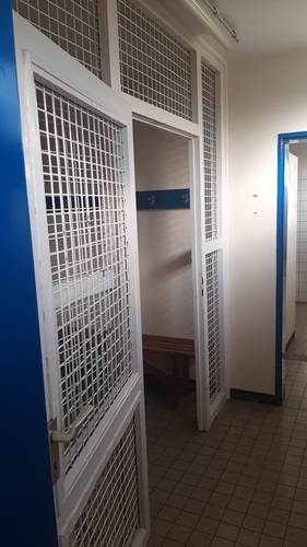 Die Turnhalle der alten Schule wird vom SV Blau-Weiß Eickelborn (WTTV) genutzt, die Umkleiden sind durch Gittertüren zu begehen, ähnlich wie in einem Forensik-Saal. (©Verein)